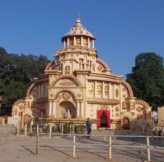 a large building with a dome on top in the middle of a dirt field next to trees