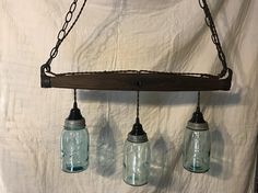 three mason jars hanging from a chain on a white sheeted wall with two lights attached to them