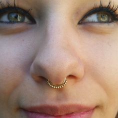 a woman's nose has a gold nose ring on it and is looking at the camera