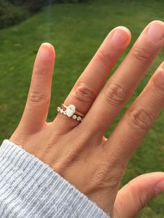 a woman's hand with an engagement ring on top of her finger, in front of a grassy area