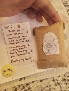 someone is holding a small bag with a note on it next to a smiley face stamp