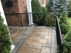 a black iron balcony railing on a brick home's front porch with trees and shrubs in the background