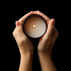 two hands holding a lit candle against a black background