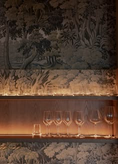 wine glasses are lined up on a shelf in front of a wallpapered wall