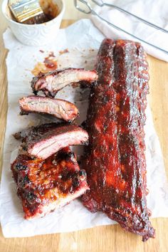 barbecue ribs are sitting on wax paper next to a cup