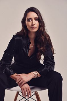 a woman sitting on top of a white chair wearing a black suit and gold watch