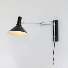 a black wall light with a white shade on it's side and a cord attached to the arm