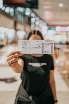 a woman is holding up a ticket in her hand while standing outside an indoor mall