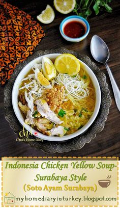 a bowl of chicken noodle soup with lemons and herbs on the side next to a spoon