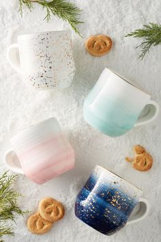 three coffee mugs sitting on top of snow covered ground next to cookies and sprinkles