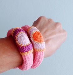 a hand holding two crocheted bracelets on it's left wrist, with an orange and pink heart in the center