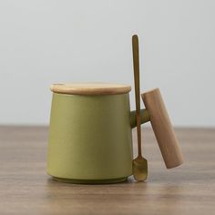 a green cup with a wooden spoon in it on top of a wood table next to a metal container