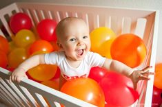 a baby in a crib with balloons all over it's body and smiling