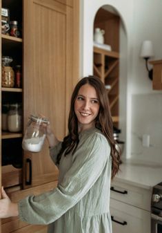 a woman standing in front of a kitchen counter holding a glass container filled with liquid