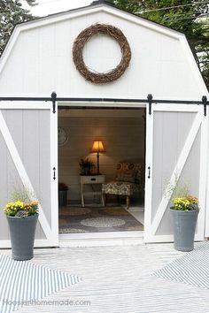 the inside of a white barn with a wreath on it's door and two potted plants