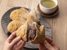 a person is holding up some cookies on a plate next to a cup of tea