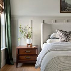 a bed with white sheets and pillows next to a wooden night stand in a bedroom