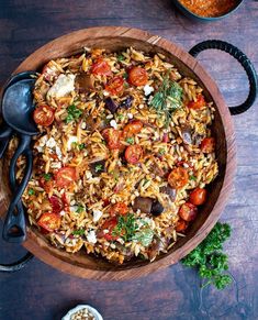 a wooden bowl filled with rice, tomatoes and other food on top of a table