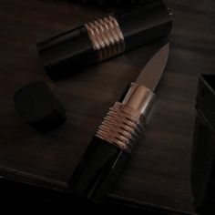 a knife and some lipstick sitting on a table next to a black box with gold trim