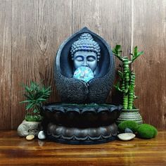 a buddha statue sitting on top of a wooden table next to some plants and rocks