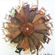 a clock made out of old metal parts on a white wall next to a tree