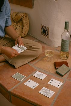 a woman is sitting on the floor playing cards with a bottle of wine in the background