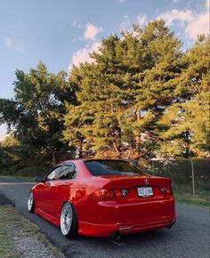 a red car is parked on the side of the road in front of some trees