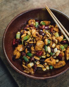 a brown bowl filled with food and chopsticks on top of a wooden table