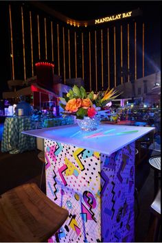 a table with flowers on it in front of a neon sign and building at night