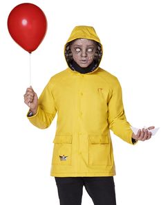 a man in a yellow raincoat holding a red balloon and wearing a mask on his face