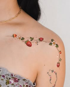 a woman's shoulder with strawberry tattoo on the left side of her arm and flower vine attached to it