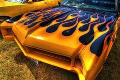 an orange car with flames painted on it's hood is parked in the grass