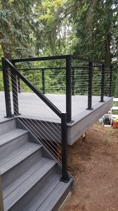 a metal hand rail on the side of a wooden deck in front of some trees