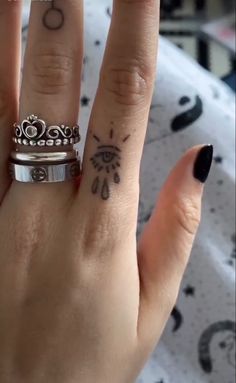 a woman's hand with two rings on it and a tattoo design on the middle finger