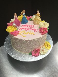 there is a birthday cake with princess figures on the frosting and flowers around it