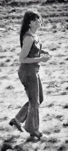 a woman walking across a sandy field holding a frisbee in her right hand