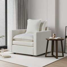 a living room with a white chair and side table in front of the window that has blinds on it