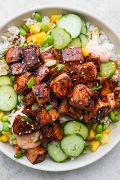 a white bowl filled with chicken, rice and cucumber on top of a table