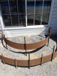 an outdoor garden bed made out of metal rods and wood strips, sitting in front of a house