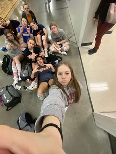 a group of young women sitting on the floor with their arms in the air and one woman taking a selfie