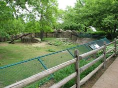 a wooden fence in front of a grassy area with trees and rocks on the other side