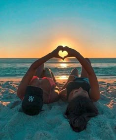 two people laying in the sand making a heart shape