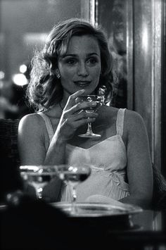 a woman sitting at a table with a glass in her hand and looking into the distance