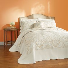 a bedroom with an orange wall and white bedding on the wooden floor next to a small table