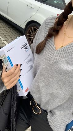 a woman sitting on the ground reading a paper with her hands in her pockets and holding a cell phone