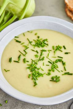 a white bowl filled with soup next to bread and green onions on a table top