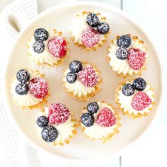 small cupcakes decorated with berries and blueberries on a white plate, ready to be eaten