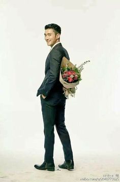 a man in a suit and tie holding a bouquet of flowers on his back while standing against a white background