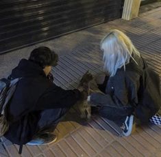 two people are sitting on the ground with their dogs and one is petting them