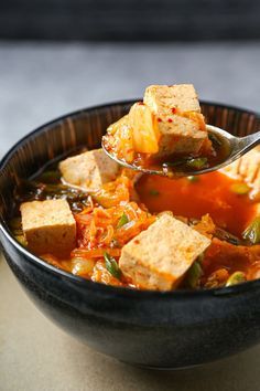 a spoon full of soup with tofu and vegetables